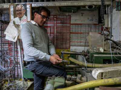 Il signore si posiziona ora dietro al lungo bancone per mostrarci il suo lavoro quotidiano. Parte piegando un fil di ferro con la sola forza delle mani...